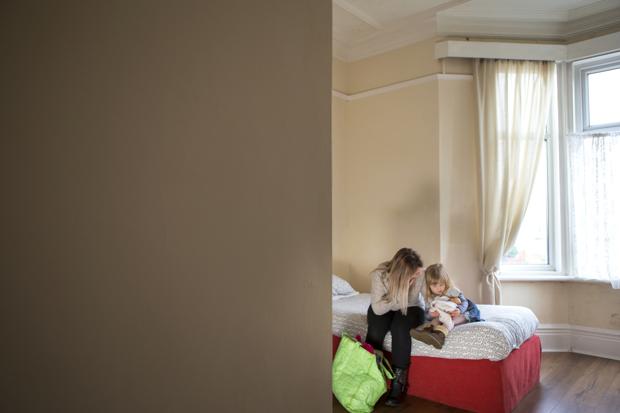 A woman and child sitting on a bed in a relatively empty room